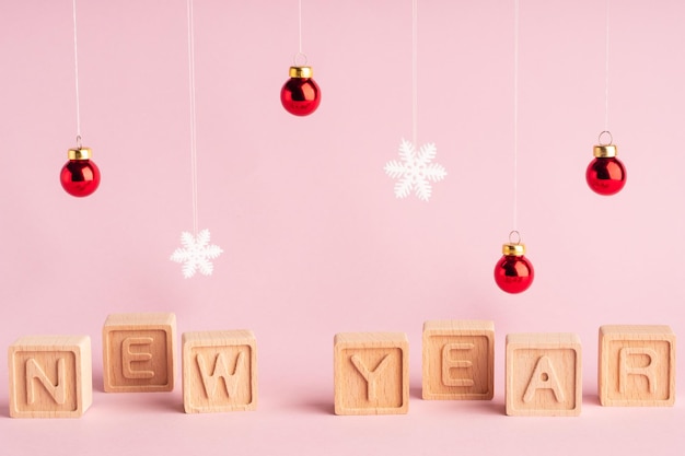 L'iscrizione nuovo anno è composta da lettere su cubi di legno Sfondo rosa e giocattoli dell'albero di Natale su una stringa