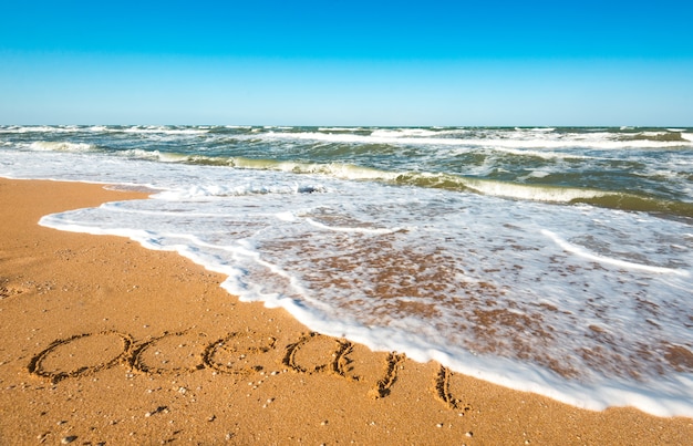 L'iscrizione sull'estate di sabbia vicino all'onda del mare tempestoso in una calda giornata estiva di sole. Concetto delle tanto attese vacanze estive e vacanze