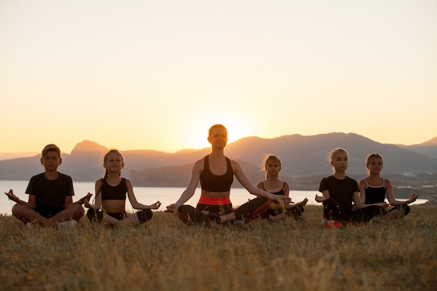 L'istruttore forma i bambini di yoga nelle montagne sull'oceano.