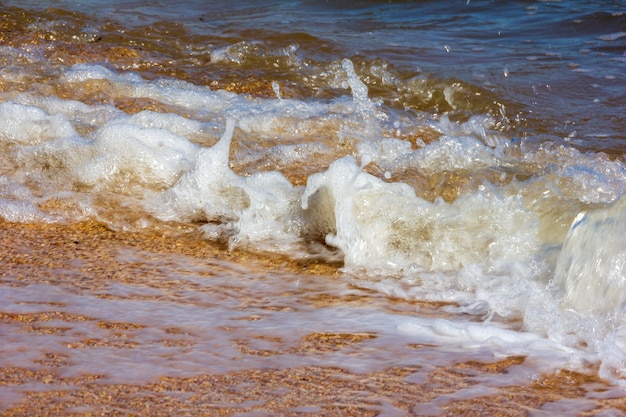 L'onda schiumosa del mare rotola sulla riva sabbiosa della spiaggia in una giornata di sole estivo