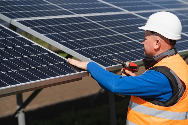 L'operaio della centrale solare con la chiave elettrica nelle sue mani ispeziona i pannelli