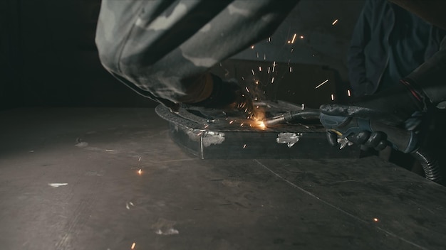 L'operaio della fucina dell'officina della fucina in un casco del cappuccio di saldatura salda una parte mediante la saldatura elettrica le scintille sono re