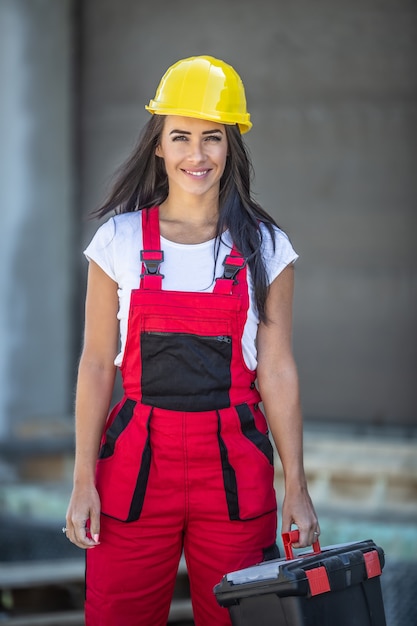 L'operaio edile femminile in tuta e casco tiene una cassetta degli attrezzi all'aperto.