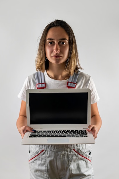 L'operaio edile femminile tiene in mano un computer portatile isolato su uno sfondo bianco