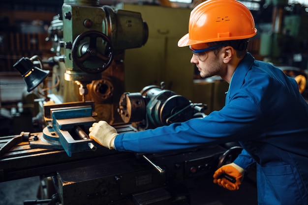 L'operaio in uniforme e casco lavora al tornio, pianta. Produzione industriale, ingegneria della lavorazione dei metalli, produzione di macchine elettriche