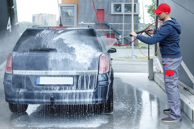 L'operaio professionista dell'autolavaggio sta lavando l'auto del cliente