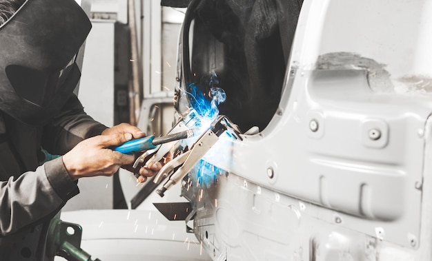 L'operatore in maschera protettiva salda gli elementi metallici dell'auto della carrozzeria Lavorando con la saldatura ad anidride carbonica