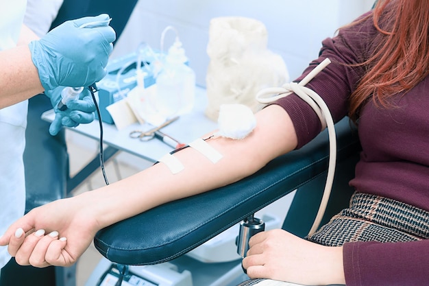 L'operatore sanitario preleva il sangue dalla vena della donna Argomento della donazione Donatore femminile seduto sulla sedia medica Mano femminile con contagocce di primo piano