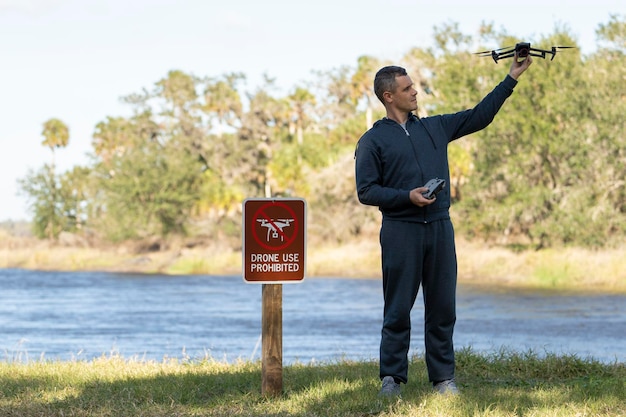 L'operatore si sta preparando a far volare il suo quadricottero nel parco nazionale senza area drone Uomo che usa illegalmente il suo UAV vicino al cartello di avviso di restrizione