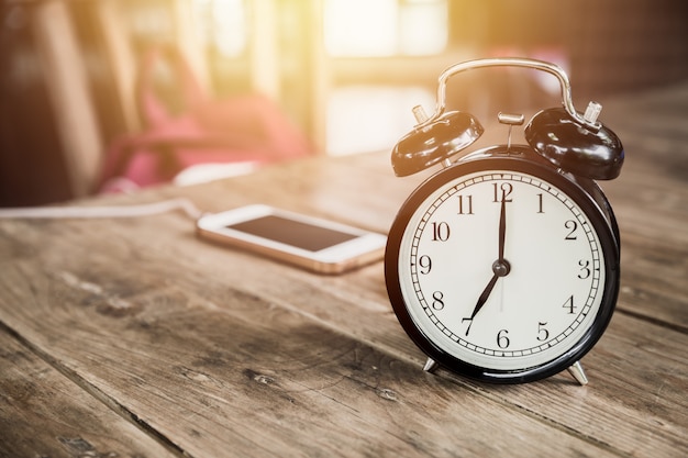 L&#39;orologio cronometra alle 7 in punto sulla tavola di legno con lo Smart Phone che si carica al fondo della sfuocatura del caffè.