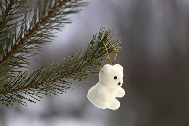 L'orsacchiotto bianco giocattolo di Capodanno è appeso a un ramo di un albero di Natale nel bosco. Foto di alta qualità