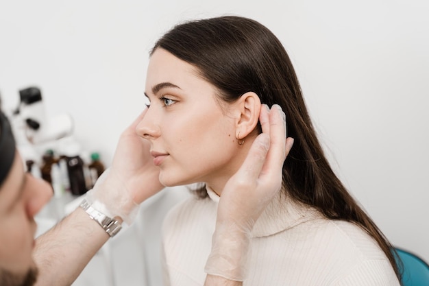 L'otoplastica è il rimodellamento chirurgico del padiglione auricolare o dell'orecchio esterno per correggere un'irregolarità e migliorare l'aspetto Il medico chirurgo esamina l'orecchio della ragazza prima della chirurgia estetica dell'otoplastica