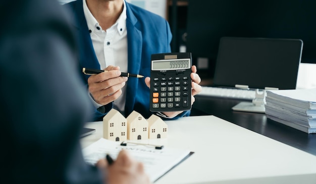 L'ufficiale di mutuo per la casa utilizza una calcolatrice con un piano casa su un tavolo di legno