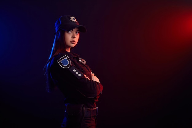 L'ufficiale di polizia femminile serio sta posando per la macchina fotografica su uno sfondo nero con rosso e blu ...