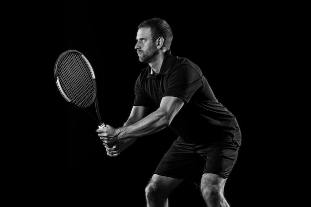 L'unico uomo caucasico che gioca a tennis isolato su sfondo nero. Studio monocromatico colpo di giovane giocatore in forma in studio in movimento o movimento durante il gioco sportivo..