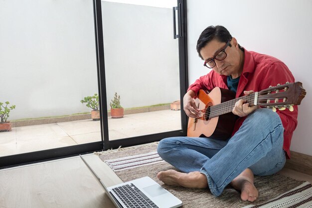 L'uomo a piedi nudi seduto su un tappeto guarda le sue note di chitarra durante le lezioni virtuali