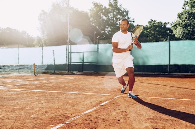 L'uomo adatto gioca a tennis sul campo da tennis