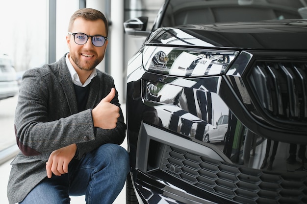 L'uomo adulto cliente maschio cliente acquirente indossa abito classico camicia bianca sceglie auto vuole comprare nuova automobile touch controllo auto in showroom veicolo salone concessionaria negozio motor show indoor Concetto di vendita