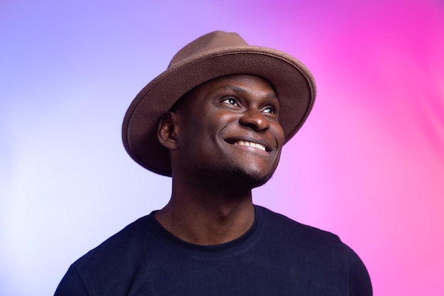 L'uomo africano americano felice sorridente indossa un cappello alla moda su sfondo rosa e viola. Concetto di festa e festa