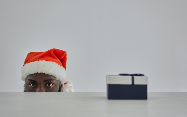 L'uomo africano con il cappello di Babbo Natale che guarda dal tavolo con un regalo