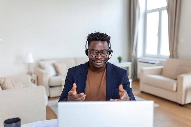 L'uomo africano concentrato indossa le cuffie con microfono guardando lo schermo del laptop