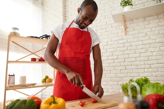 L&#39;uomo africano in grembiule affetta i pomodori in cucina.