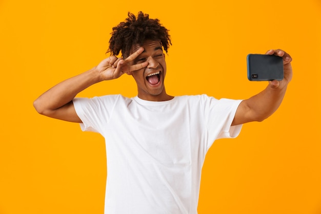 L'uomo africano in posa isolato sopra lo spazio giallo prende un selfie per telefono.