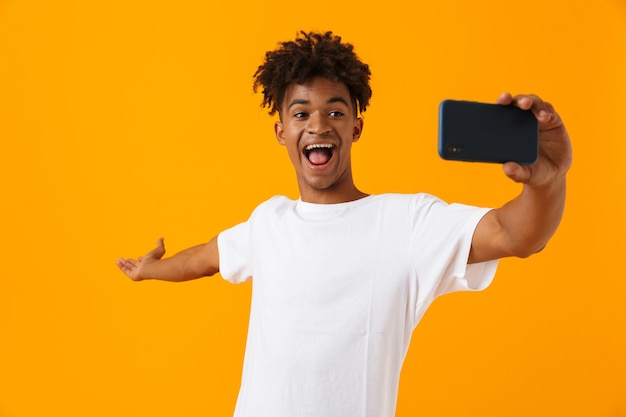 L'uomo africano in posa isolato sopra lo spazio giallo prende un selfie per telefono.