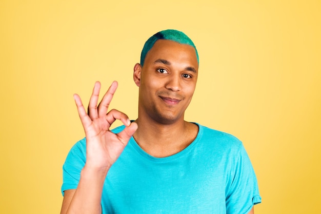 L'uomo africano nero in casual sullo sguardo felice della parete gialla alla macchina fotografica con il gesto giusto di manifestazione di sorriso