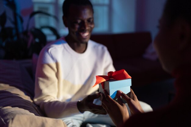 L'uomo africano riceve un regalo inaspettato dalla moglie a casa, una donna che regala una confezione regalo al fidanzato felice