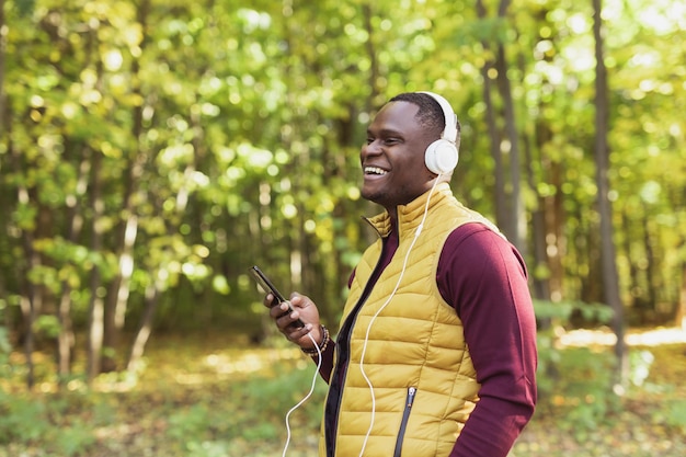 L'uomo afroamericano ascolta la musica nello spazio della copia del parco di primavera e nel luogo per l'app del gadget pubblicitario