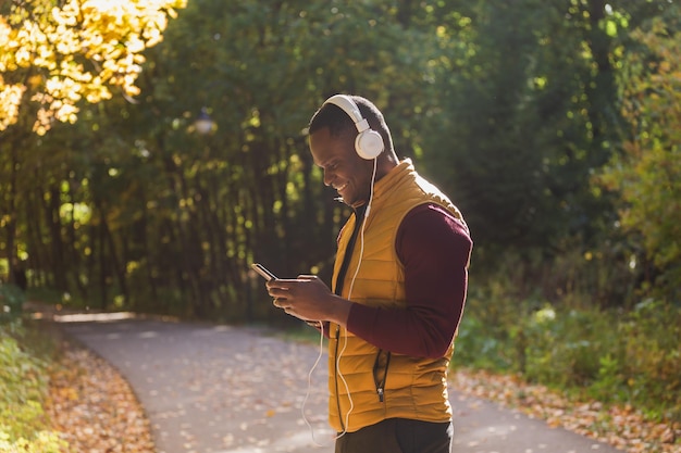 L'uomo afroamericano ascolta musica nello spazio della copia del parco autunnale e luogo per la pubblicità App gadget e concetto di servizio di streaming