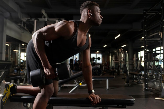 l'uomo afroamericano atletico si allena in palestra al buio. Il ragazzo atletico solleva manubri pesanti nel fitness club