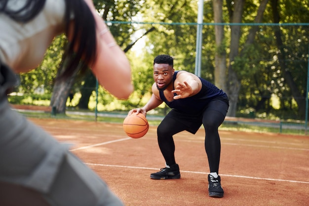 L'uomo afroamericano con la ragazza gioca a basket sul campo all'aperto