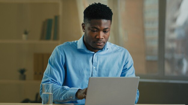 L'uomo afroamericano dell'uomo d'affari che lavora al computer nell'ufficio domestico fa la pausa bevendo il bicchiere di
