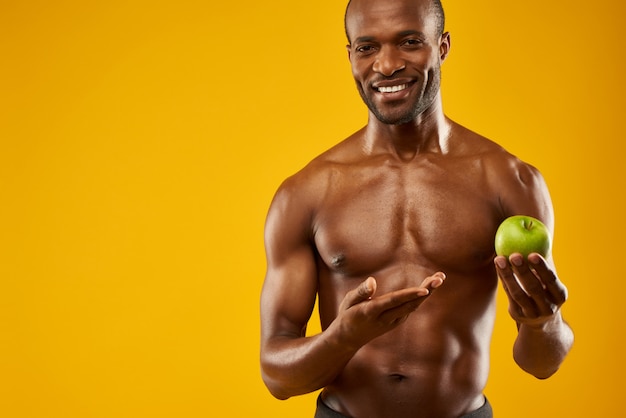 L'uomo afroamericano felice con il torso nudo tiene la mela.