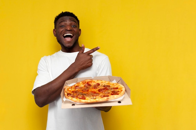 l'uomo afroamericano felice in maglietta bianca tiene una scatola di pizza e mostra la mano di lato