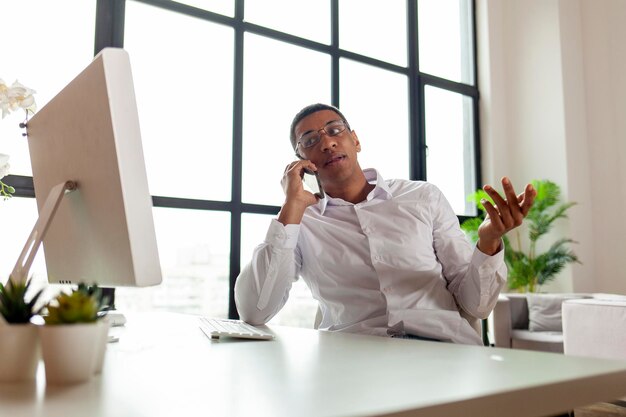 L'uomo afroamericano in abiti da lavoro e occhiali si siede al computer in ufficio a parlare