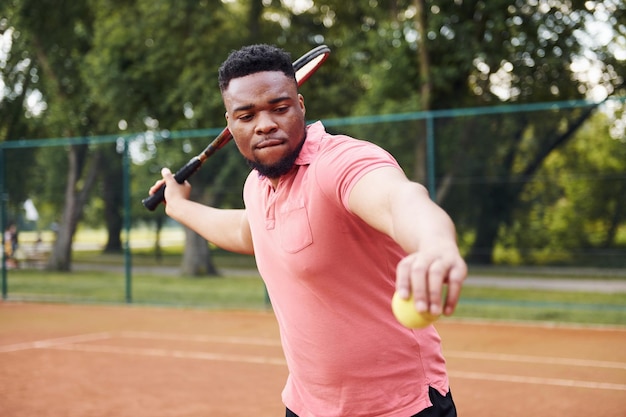 L'uomo afroamericano in camicia rosa gioca a tennis sul campo all'aperto