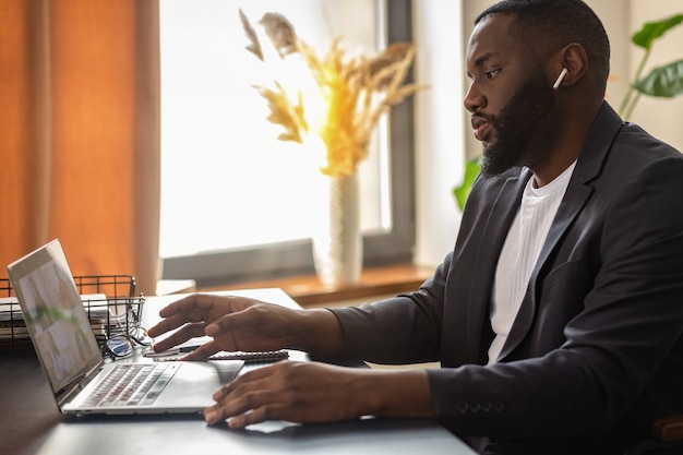 L'uomo afroamericano sta partecipando a una conferenza online seduto al tavolo di casa. Lavoro a distanza, concetto di autoisolamento