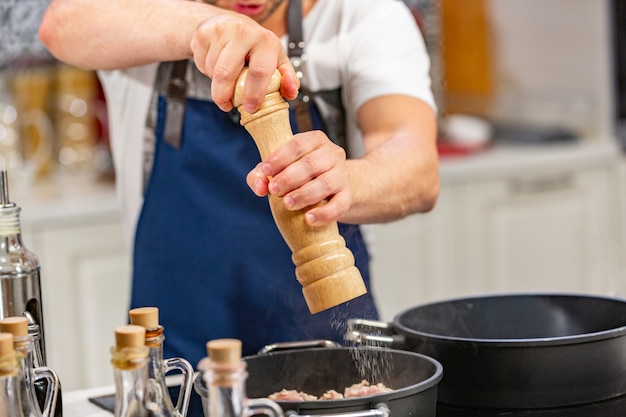 L'uomo aggiunge pepe macinato dal mulino nella padella sul fornello. concetto di ooking