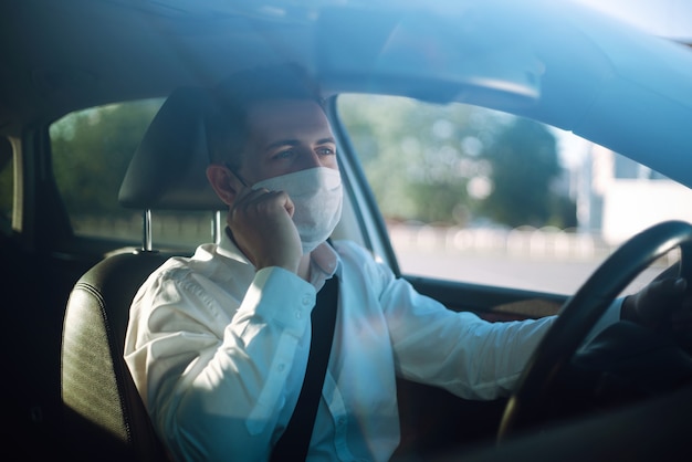 L'uomo alla guida di un'auto indossa una mascherina medica durante un'epidemia nella città di quarantena.