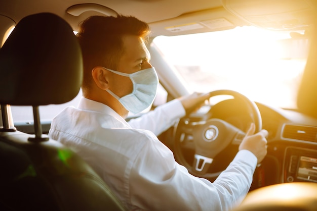 L'uomo alla guida di un'auto indossa una mascherina medica durante un'epidemia nella città di quarantena.