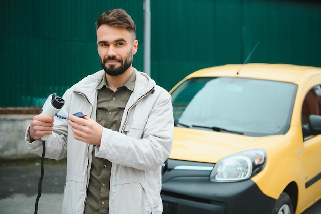 L'uomo alla moda inserisce il cavo di ricarica nella presa dell'auto elettrica