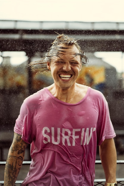 L'uomo allegro con una maglietta luminosa con uno skateboard in uno skatepark ride, gli schizzi d'acqua dai capelli.