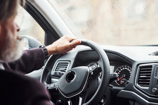 L'uomo anziano alla moda in abiti eleganti è nell'auto moderna.