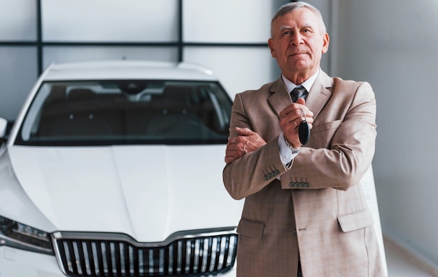 L'uomo anziano allegro in abbigliamento formale si trova di fronte alla moderna auto bianca.