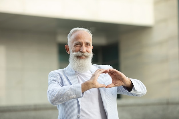 L'uomo anziano barbuto mostra il segno di amore all'aperto