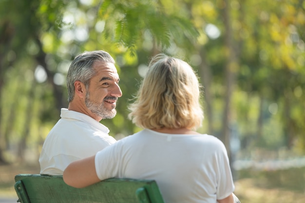 L'uomo anziano caucasico esamina la donna mentre sieda e si rilassi sui banchi nel parco pubblico concetto di uso felicemente della vita. in vacanza di coppia di anziani.