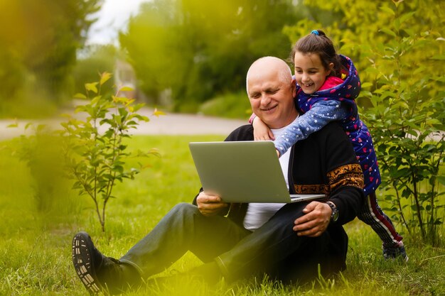 L'uomo anziano con sua nipote sta studiando un computer portatile all'aperto. Educazione su Internet per il vecchio nonno.